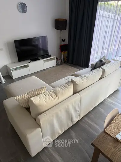 Modern living room with sleek furniture and large TV, featuring a cozy ambiance and natural light.