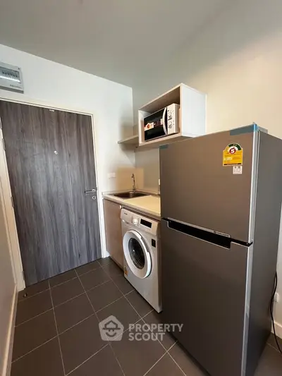 Modern kitchen with washing machine, fridge, and microwave in compact layout.