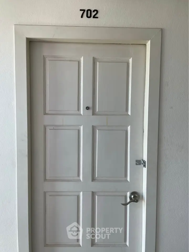 White apartment door with number 702, modern handle, and peephole.