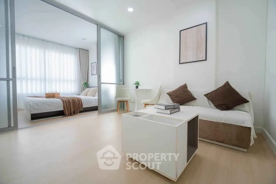 Modern open-layout living room with cozy bedroom view, featuring minimalist decor and natural light.
