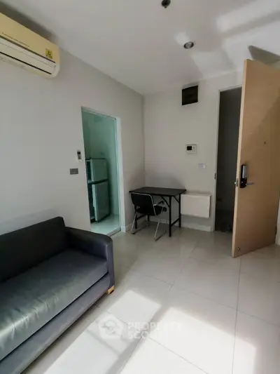 Modern apartment interior with sleek sofa, compact dining area, and visible kitchen entryway.