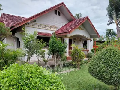 Charming single-story house with red-tiled roof and lush garden, perfect for serene living.