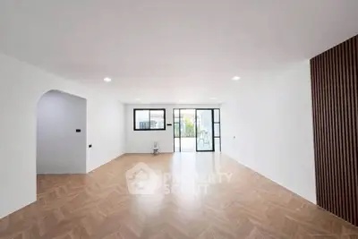 Spacious modern living room with wooden flooring and large windows opening to a balcony.