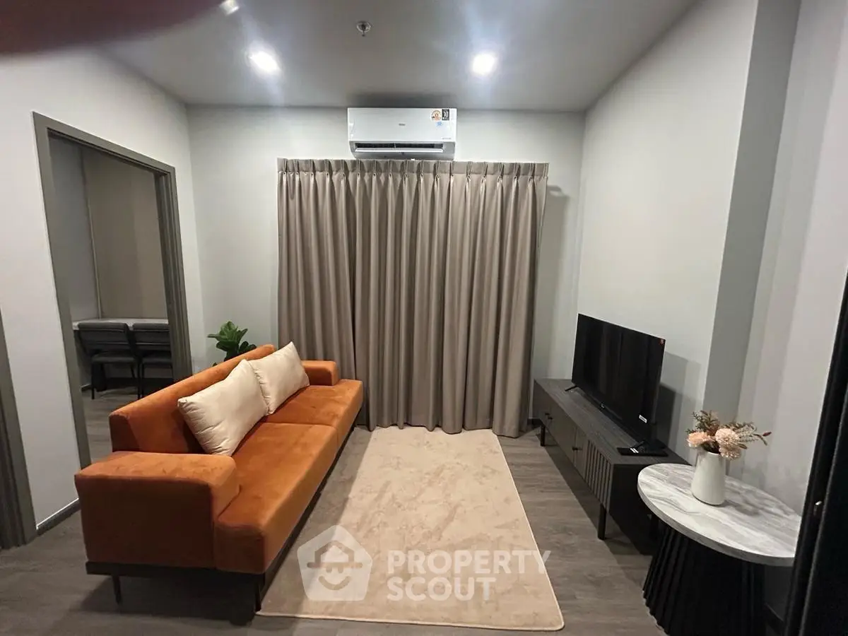 Modern living room with orange sofa, TV, and air conditioning in a cozy apartment setting.