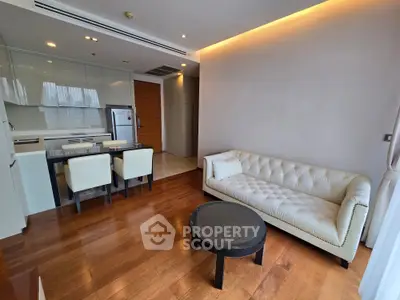 Modern living room with open kitchen, featuring elegant furniture and wooden flooring.