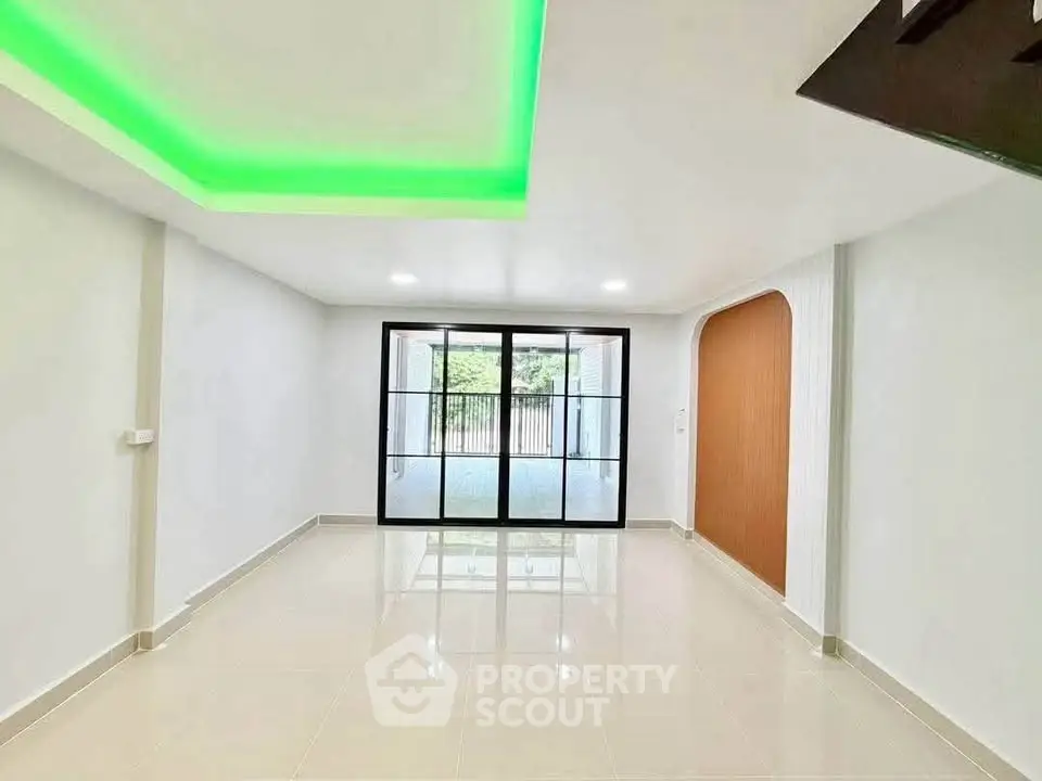 Spacious modern living room with green LED ceiling lights and large glass doors.
