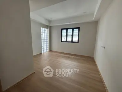 Spacious empty room with wooden flooring and large window, perfect for customization.