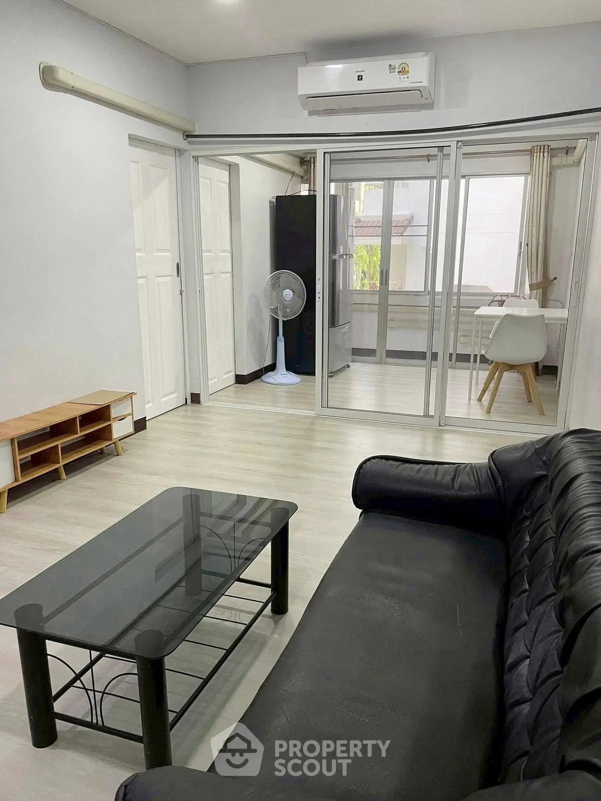 Modern living room with sleek black sofa, glass coffee table, and sliding glass doors leading to dining area.