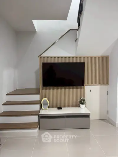 Modern minimalist living area with sleek staircase and wall-mounted TV