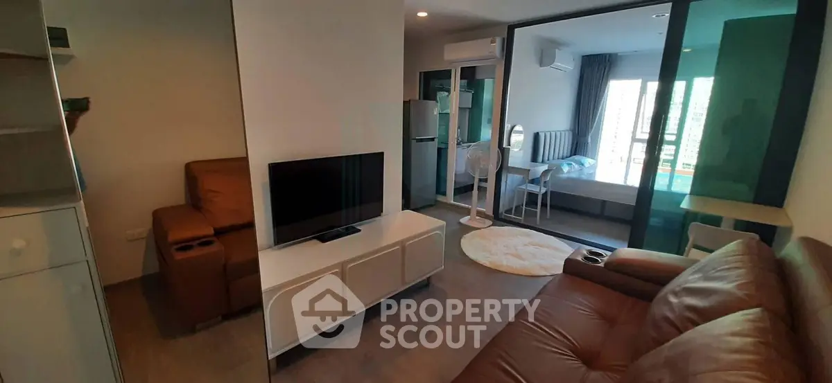 Modern living room with leather sofas and TV, open layout to bedroom with glass partition.