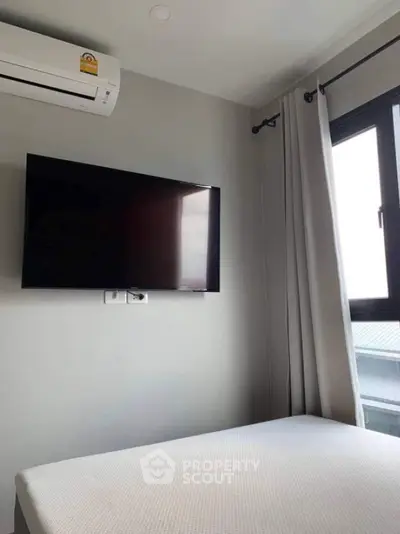 Modern bedroom with wall-mounted TV and air conditioning, featuring large window with curtains.