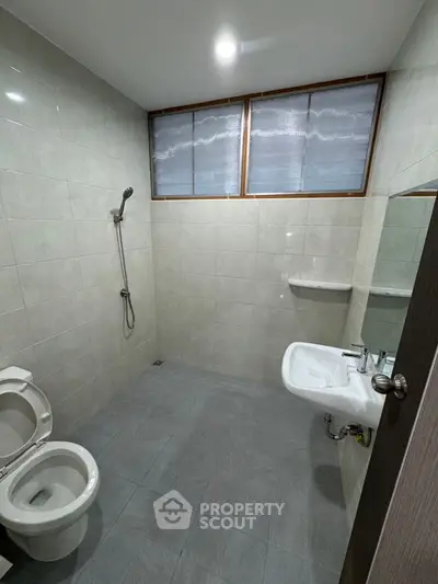 Modern bathroom with sleek fixtures and neutral tiles, featuring a shower and toilet.
