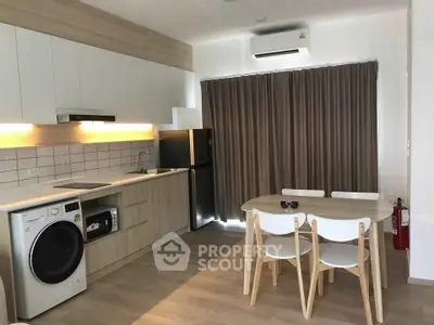 Modern kitchen with dining area, featuring sleek cabinetry, washing machine, and fridge in a cozy apartment setting.