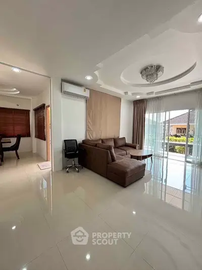 Spacious living room with modern sofa and elegant ceiling design, adjacent to dining area with natural light.