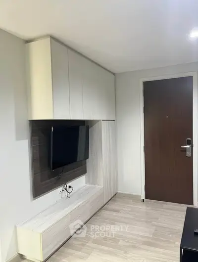 Modern living room with sleek TV unit and wooden flooring, featuring a stylish entrance door.