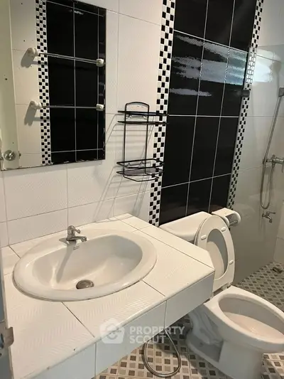 Modern bathroom with stylish black and white tiles, featuring a sink and toilet.