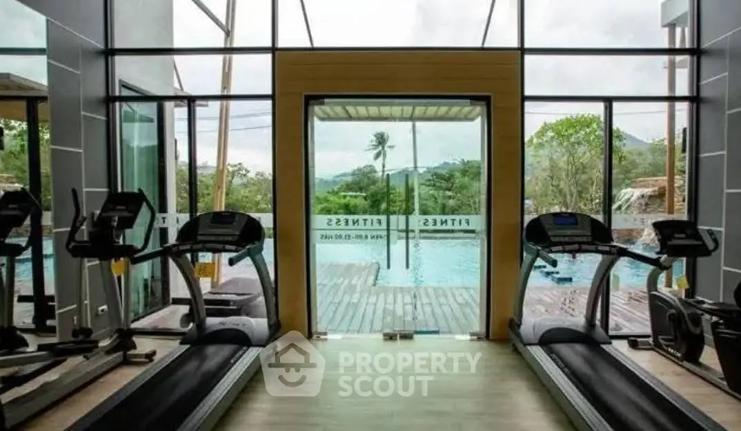 Modern gym with pool view and lush greenery, featuring state-of-the-art treadmills and floor-to-ceiling windows.