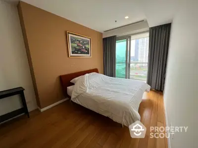 Spacious bedroom with polished wooden floors, large windows offering ample natural light, and a serene city view, perfect for relaxation and comfort.