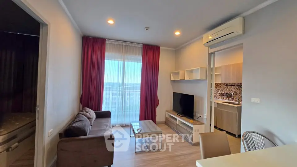 Modern living room with balcony view, featuring sleek furniture and open kitchen layout.