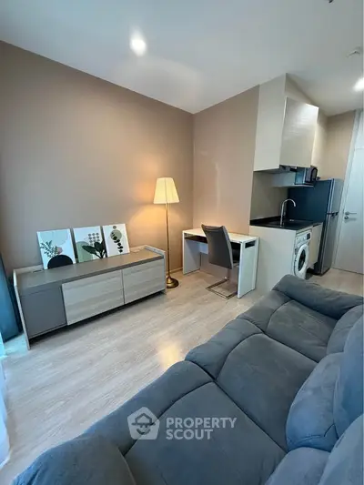 Modern living room with cozy sofa, stylish decor, and compact kitchen featuring washing machine.