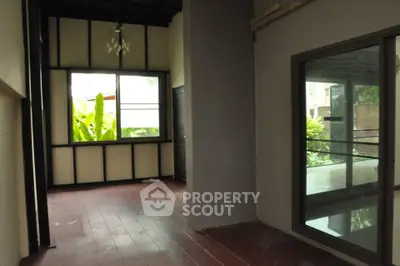 Spacious balcony with wooden flooring and large windows overlooking lush greenery.