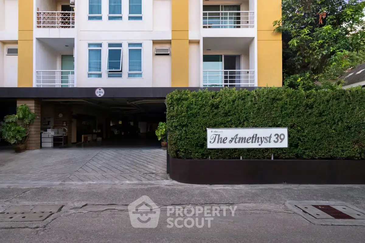 Modern apartment building entrance with lush greenery and stylish facade.