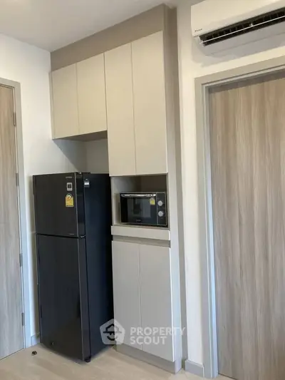 Modern kitchen with sleek cabinetry, refrigerator, and microwave in a compact layout.