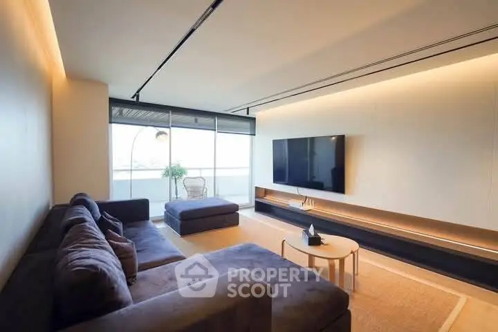 Spacious modern living room with large sofa and wall-mounted TV, featuring a sleek design and natural lighting.