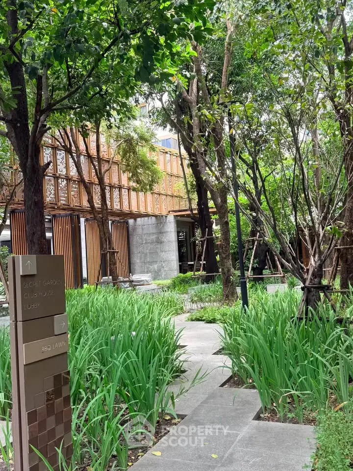 Lush garden pathway leading to a modern building with wooden accents, perfect for serene living.