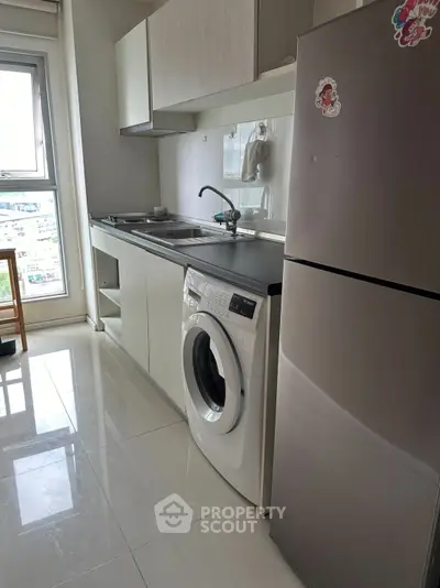 Modern kitchen with sleek appliances and city view, featuring washing machine and fridge.