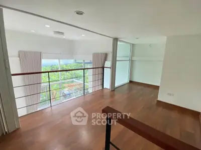 Spacious loft with wooden flooring and large windows offering lush green views.