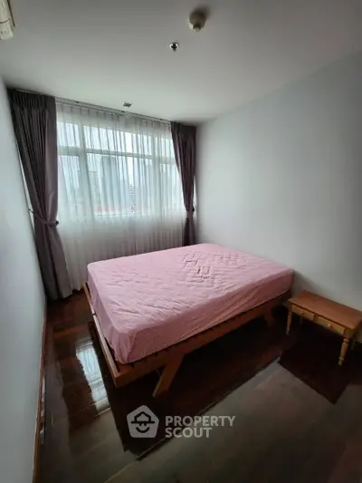 Cozy bedroom with large window and wooden flooring, featuring a neatly made bed and soft lighting.