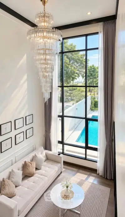 Luxurious living room with high ceiling, elegant chandelier, and large window overlooking a pool.