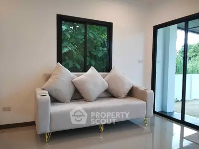 Modern living room with elegant sofa and large windows offering natural light and garden view.
