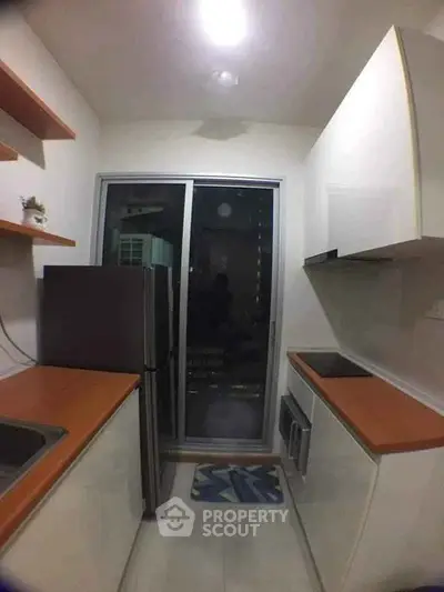 Modern compact kitchen with sleek cabinetry and wooden countertops, featuring a sliding glass door for natural light.