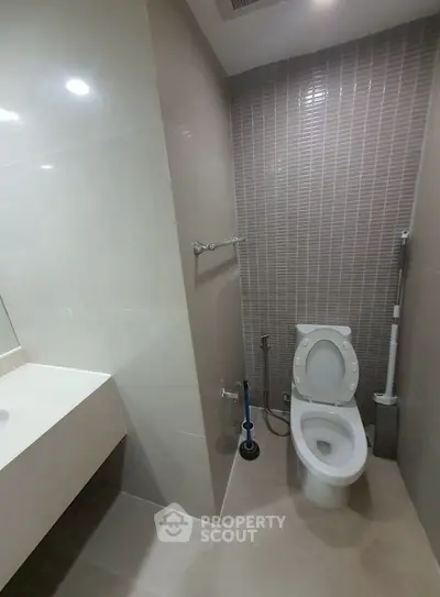 Modern bathroom with sleek design and tiled walls, featuring a toilet and vanity area.