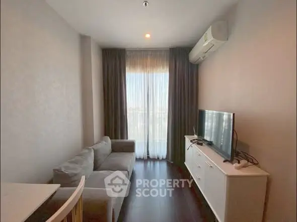 Cozy living room with modern sofa and TV, featuring large window with curtains.