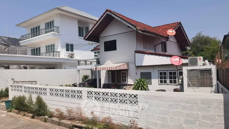 Charming two-story house with red roof and satellite dishes, nestled in a serene neighborhood.