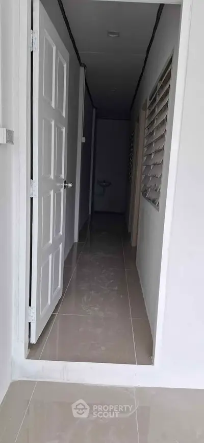 Modern hallway with sleek tiled flooring and white doors, leading to a minimalist interior space.