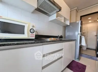 Modern kitchen with sleek cabinets, microwave, and stainless steel fridge in a compact layout.