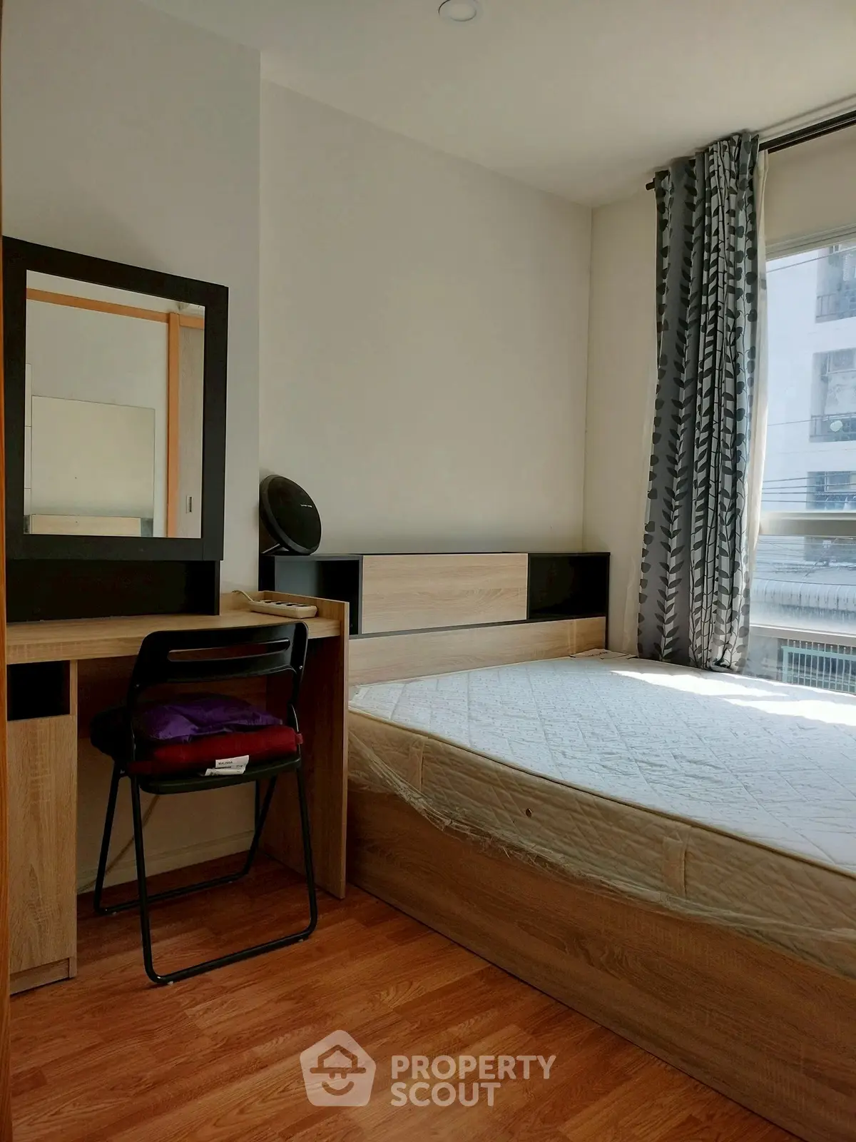 Cozy bedroom with natural light, featuring a bed, desk, and chair, ideal for comfortable living.