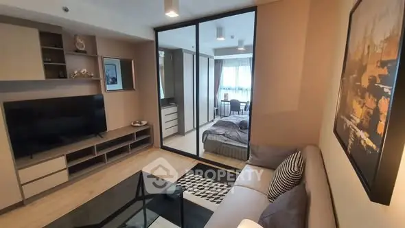 Modern living room with stylish decor and a view into a cozy bedroom, featuring sleek furniture and a large TV.
