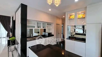 Modern kitchen with sleek black countertops and white cabinetry, featuring a stylish chandelier and open layout.