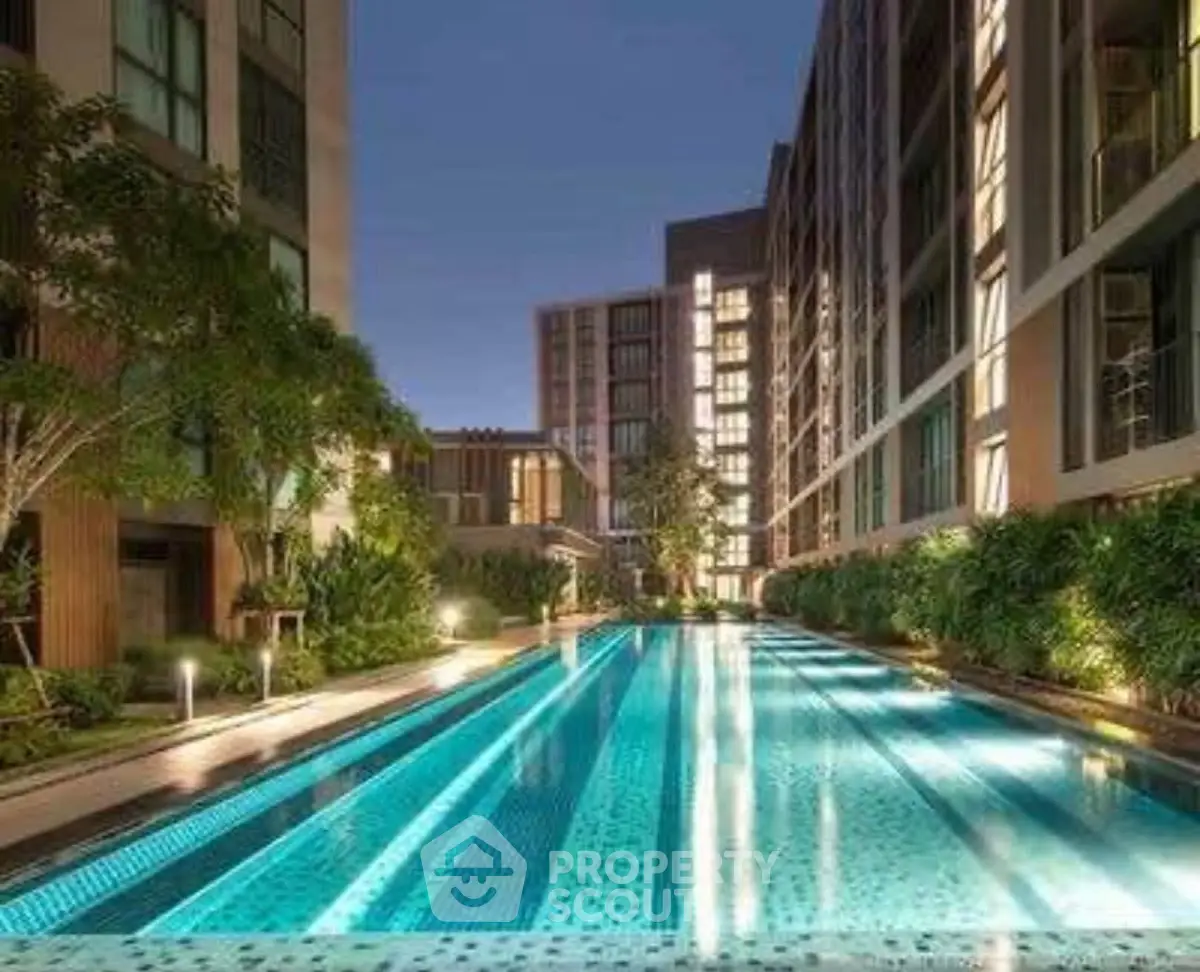 Luxurious modern apartment complex with illuminated swimming pool at night, surrounded by lush greenery.