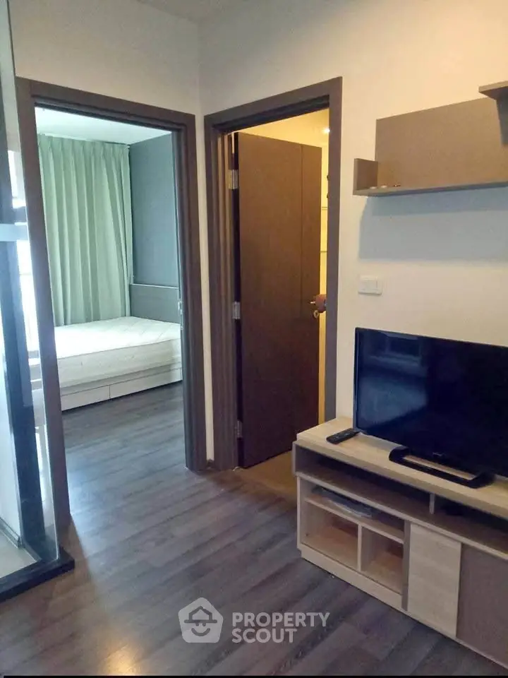 Modern apartment interior with cozy living room and adjacent bedroom, featuring sleek wooden flooring and stylish decor.
