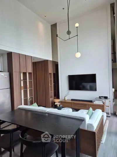 Modern living room with high ceiling, stylish furniture, and wall-mounted TV in a contemporary apartment.