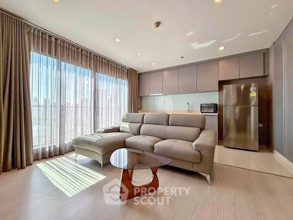 Spacious modern living room with large windows and sleek kitchen area in a high-rise apartment.