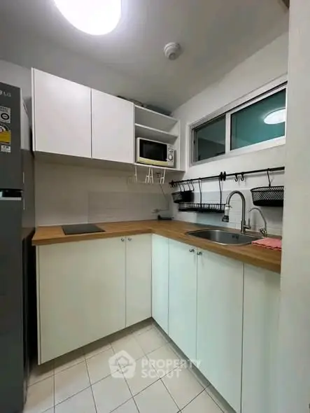 Modern compact kitchen with white cabinets and wooden countertops, featuring a microwave and sleek design.