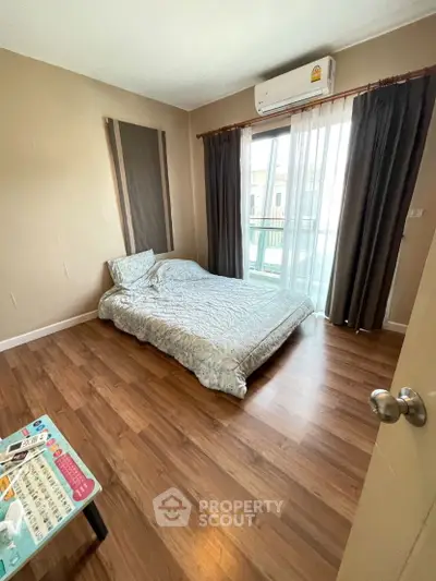 Cozy bedroom with wooden flooring and balcony access in modern apartment.
