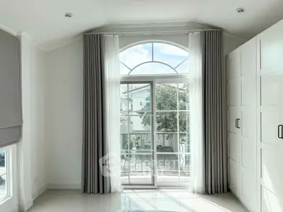 Bright bedroom with large window and elegant curtains, offering a serene view and ample natural light.